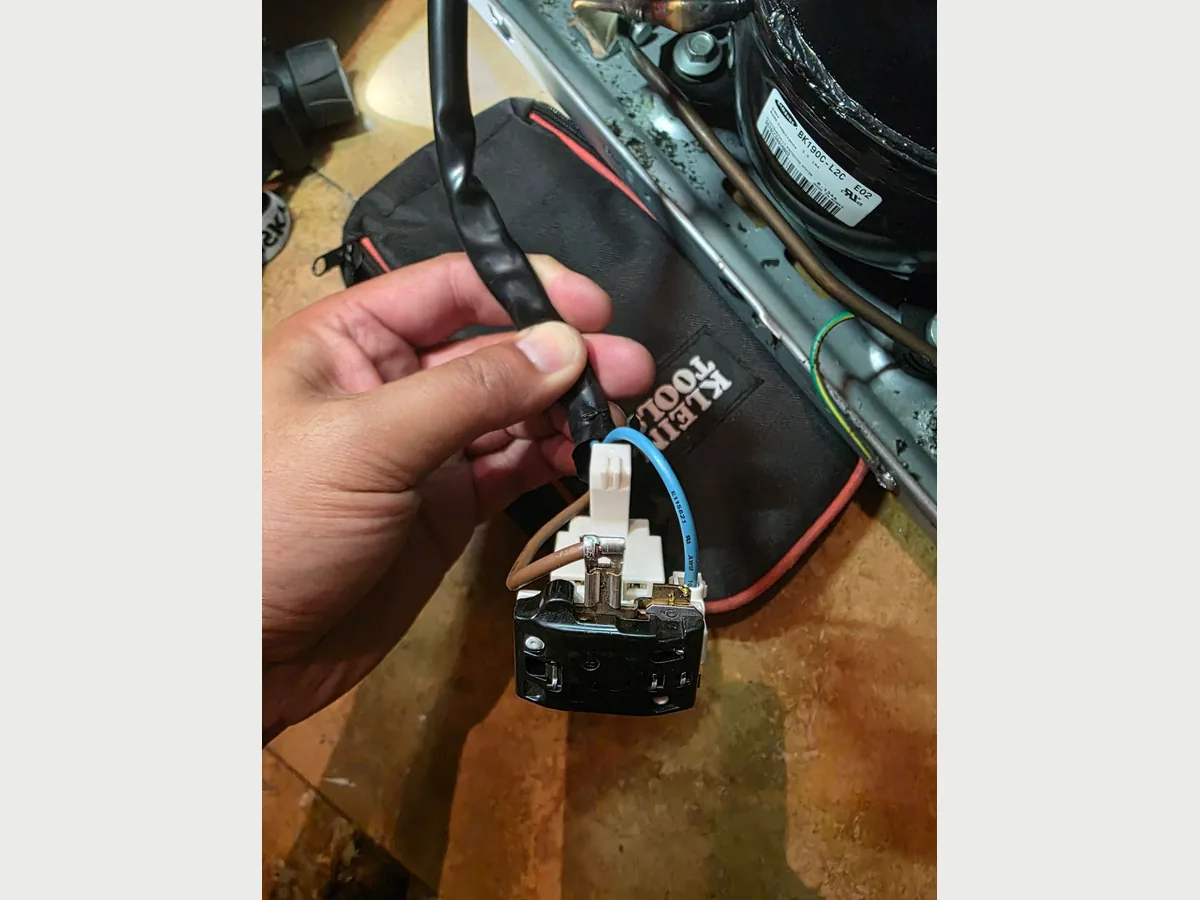Start relay held next to a refrigerator compressor